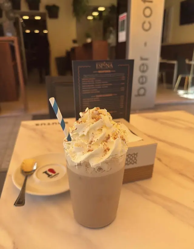 Café frío con nata y canela, con pajita de rayas azules, en una mesa de mármol