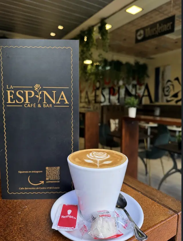 Carta negra y dorada de La Espina junto a un café con una rosa dibujada en la espuma