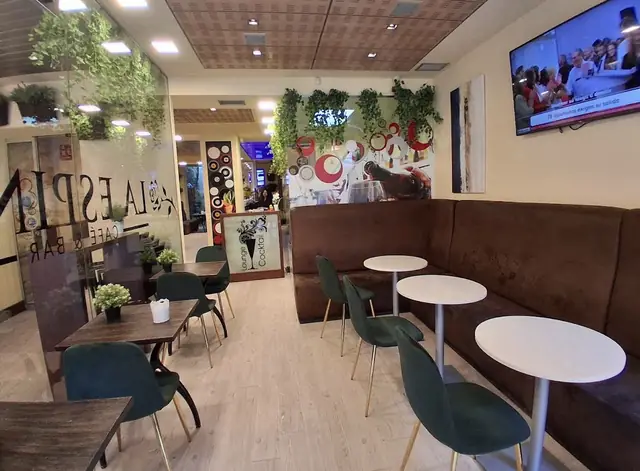 Sofá corrido, mesas redondas blancas y sillas verdes en el interior del local